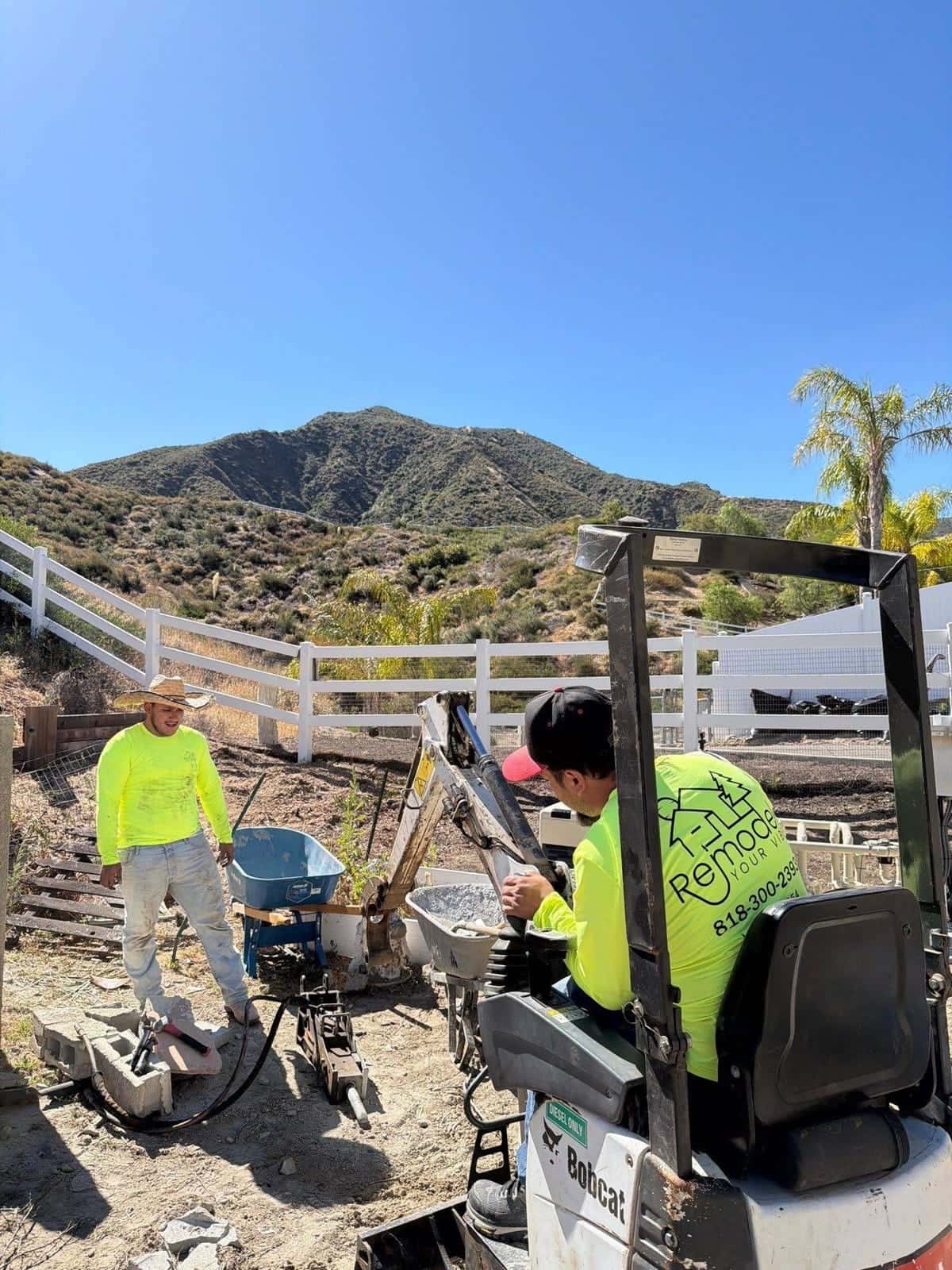 Mini excavator and crew breaking ground in a hillside backyard
