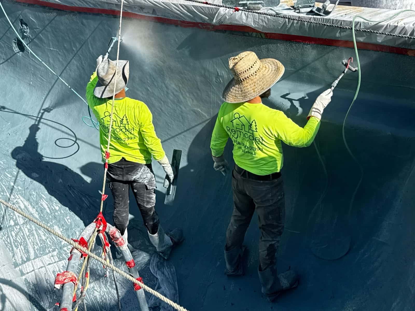 Two crew members spraying a pool wall before finishing