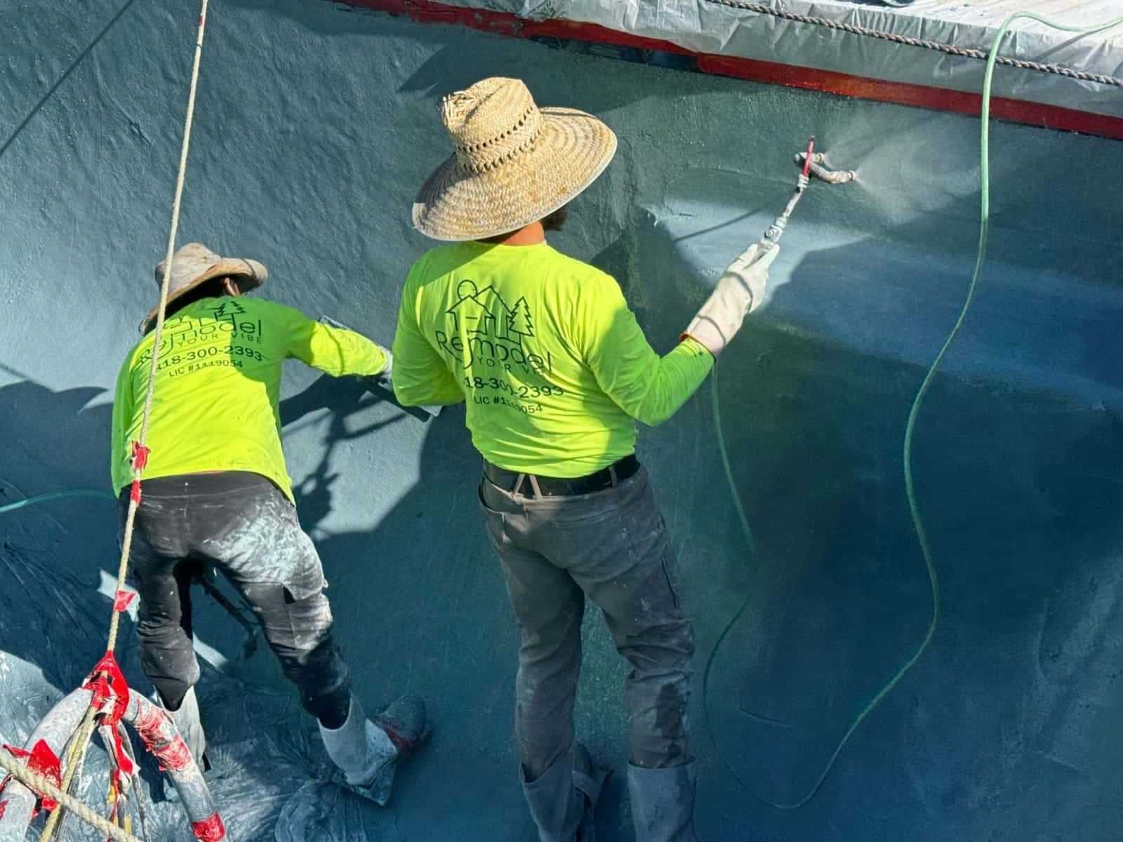 Two crew members spraying and troweling a pool wall
