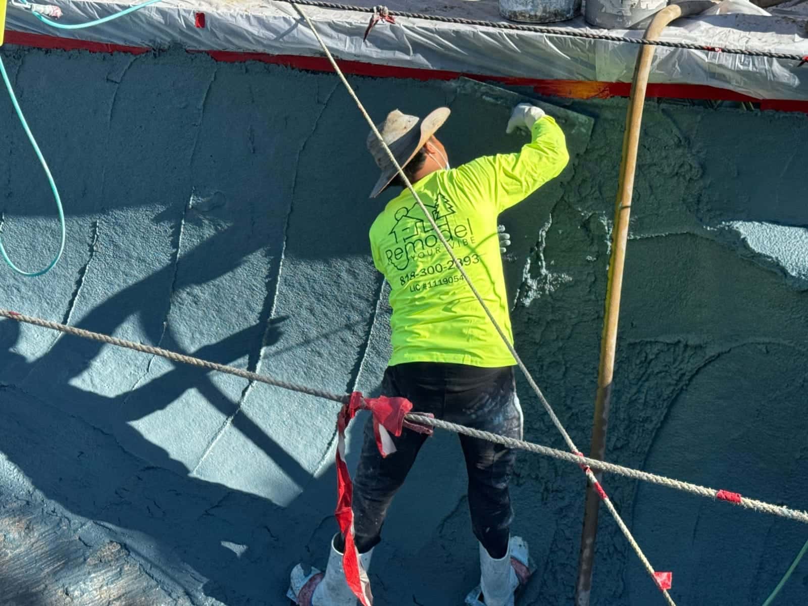 Crew member troweling plaster up a curved pool wall