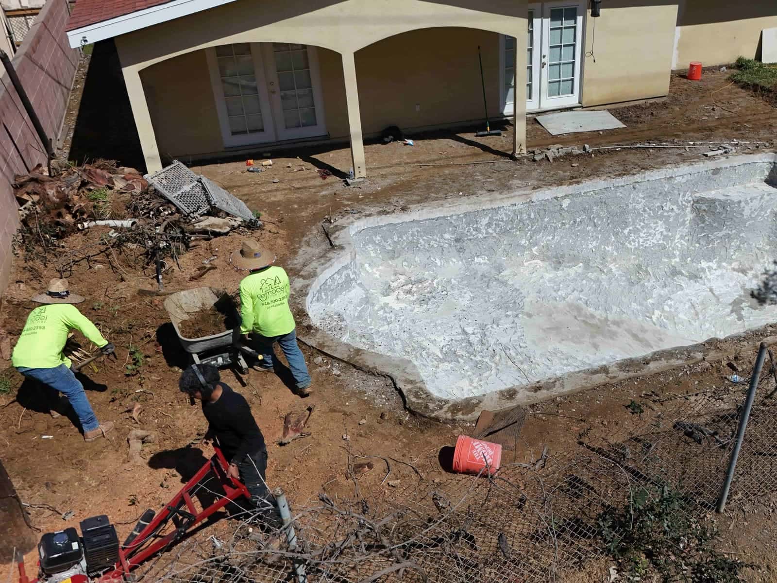 Crew clearing brush and soil beside an old pool shell before a remodel
