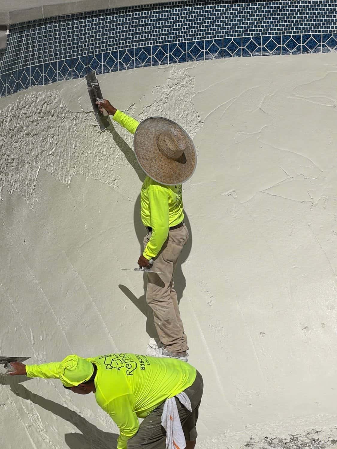 Two plasterers smoothing a pool wall below the tile