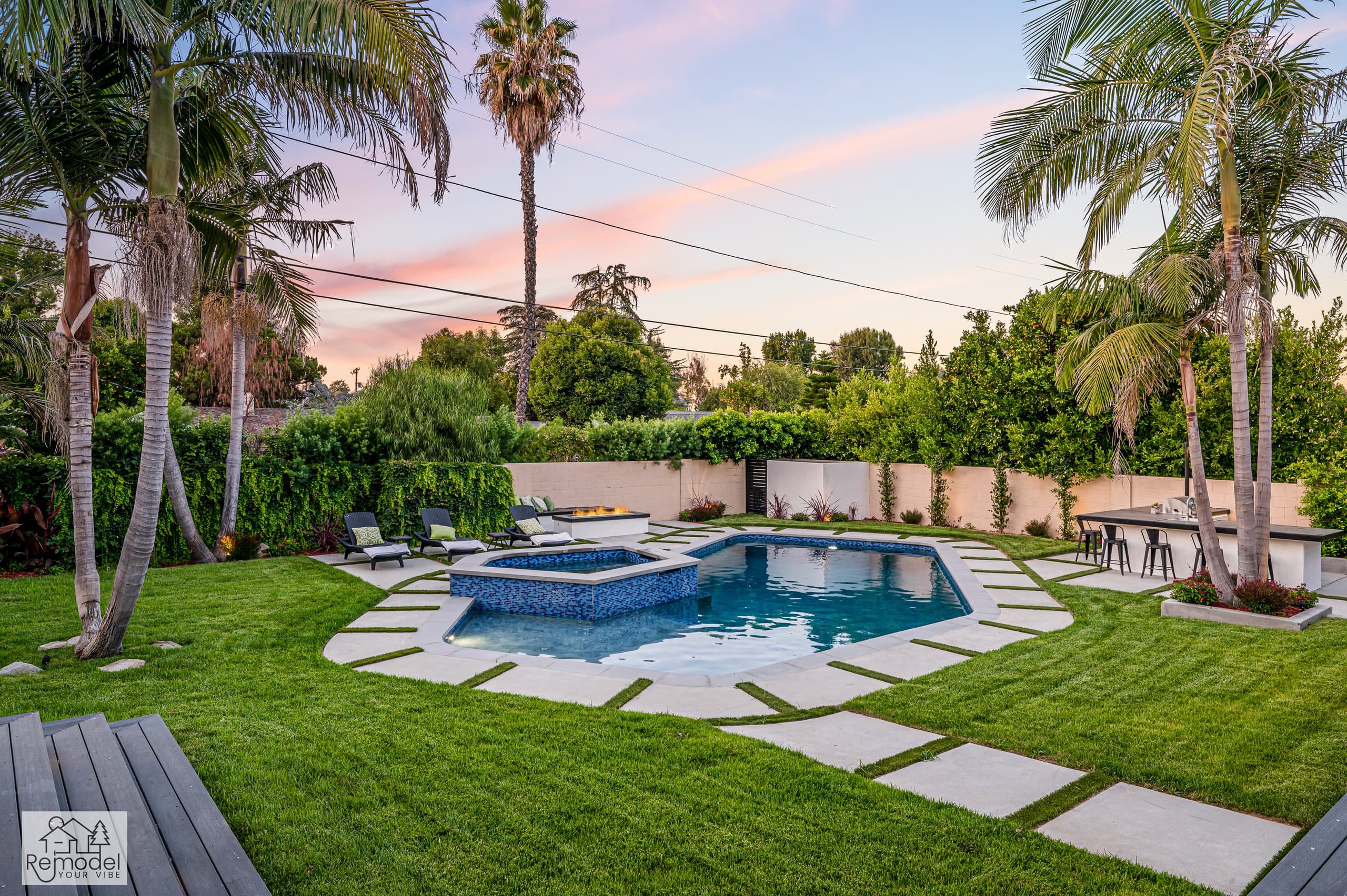 Pool and raised spa with a fire pit, outdoor bar and lawn at dusk