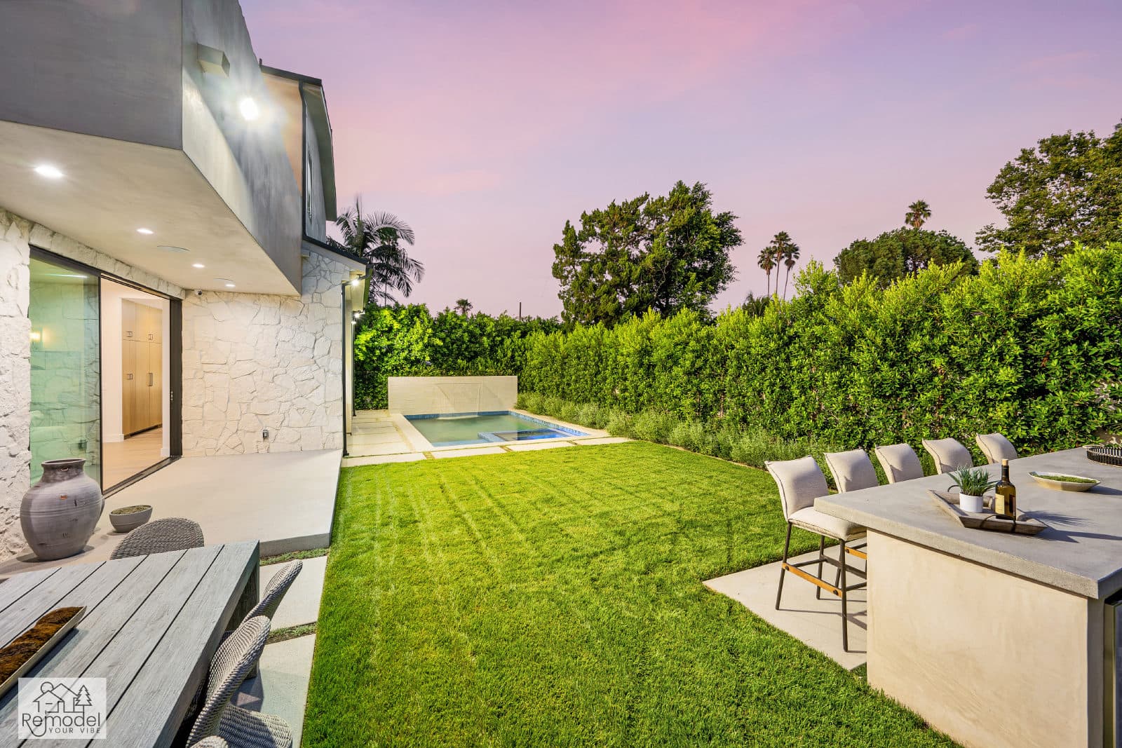 Lawn and built-in outdoor bar with stools beside a modern home at dusk