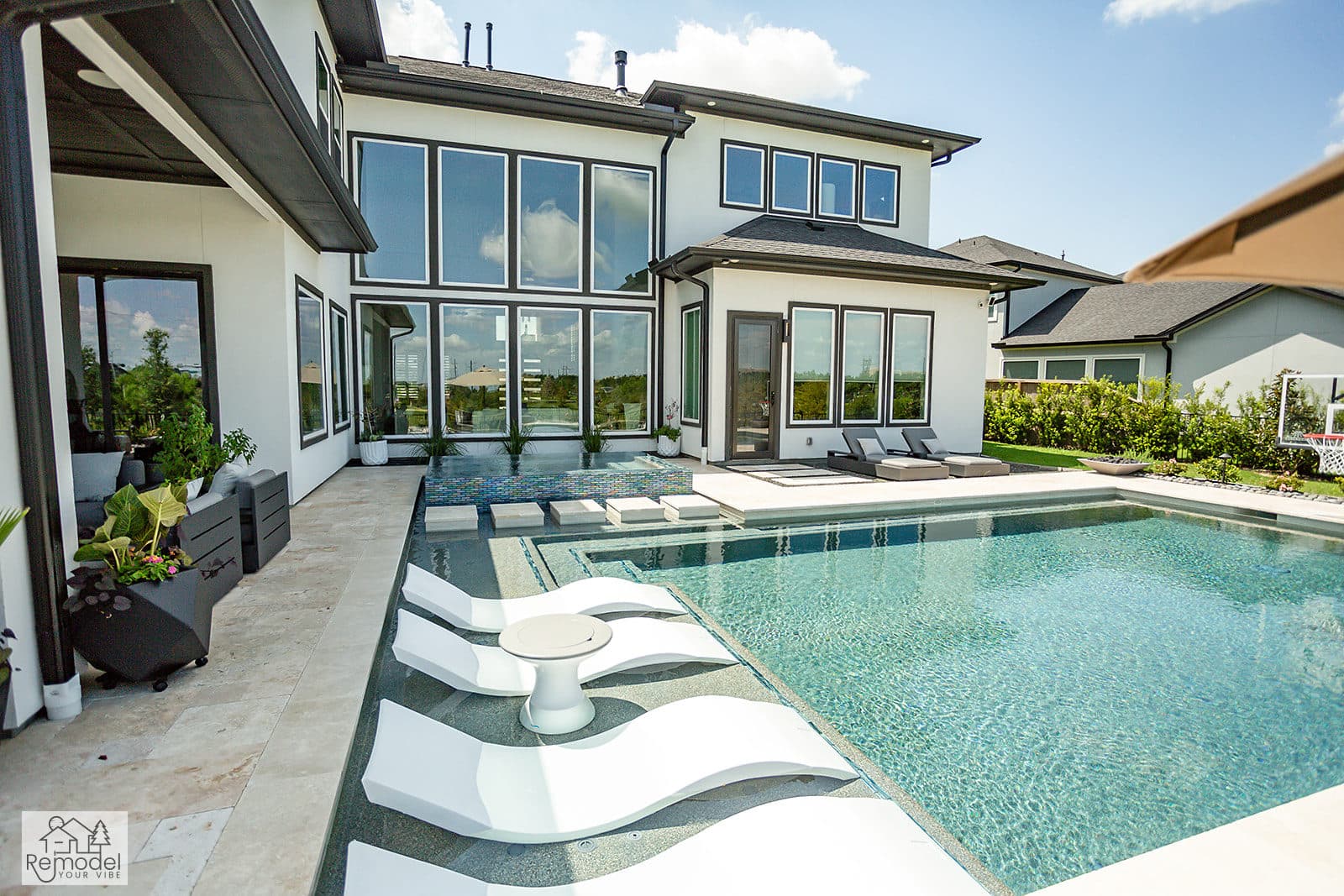 Modern pool with in-water loungers beside a two-story home