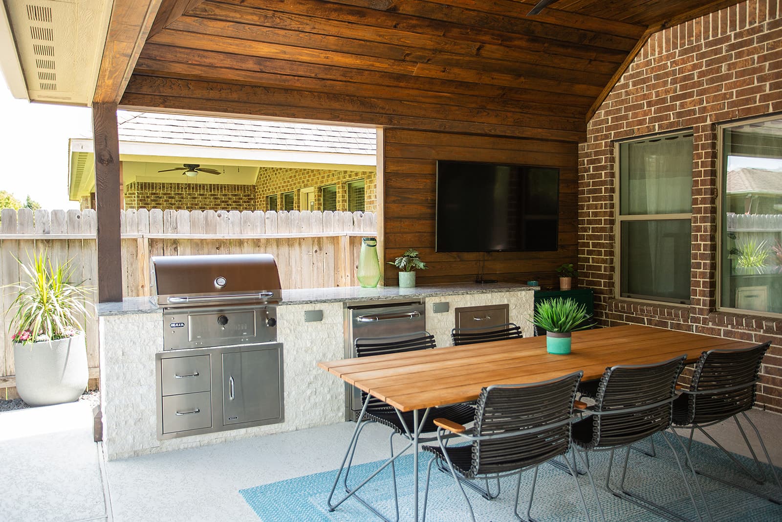 Covered outdoor kitchen with built-in grill, dining area, and TV